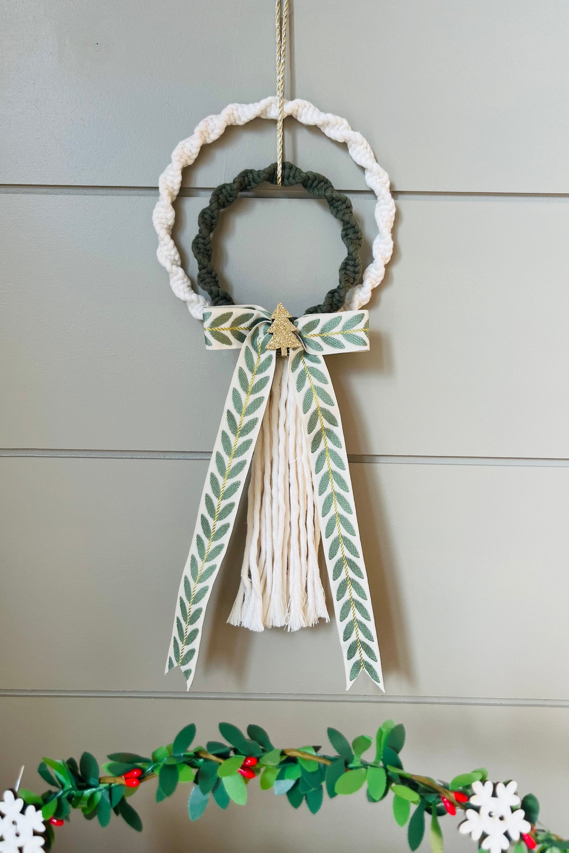 Decorative macrame Christmas wreath with tassels and a bow on a plain background