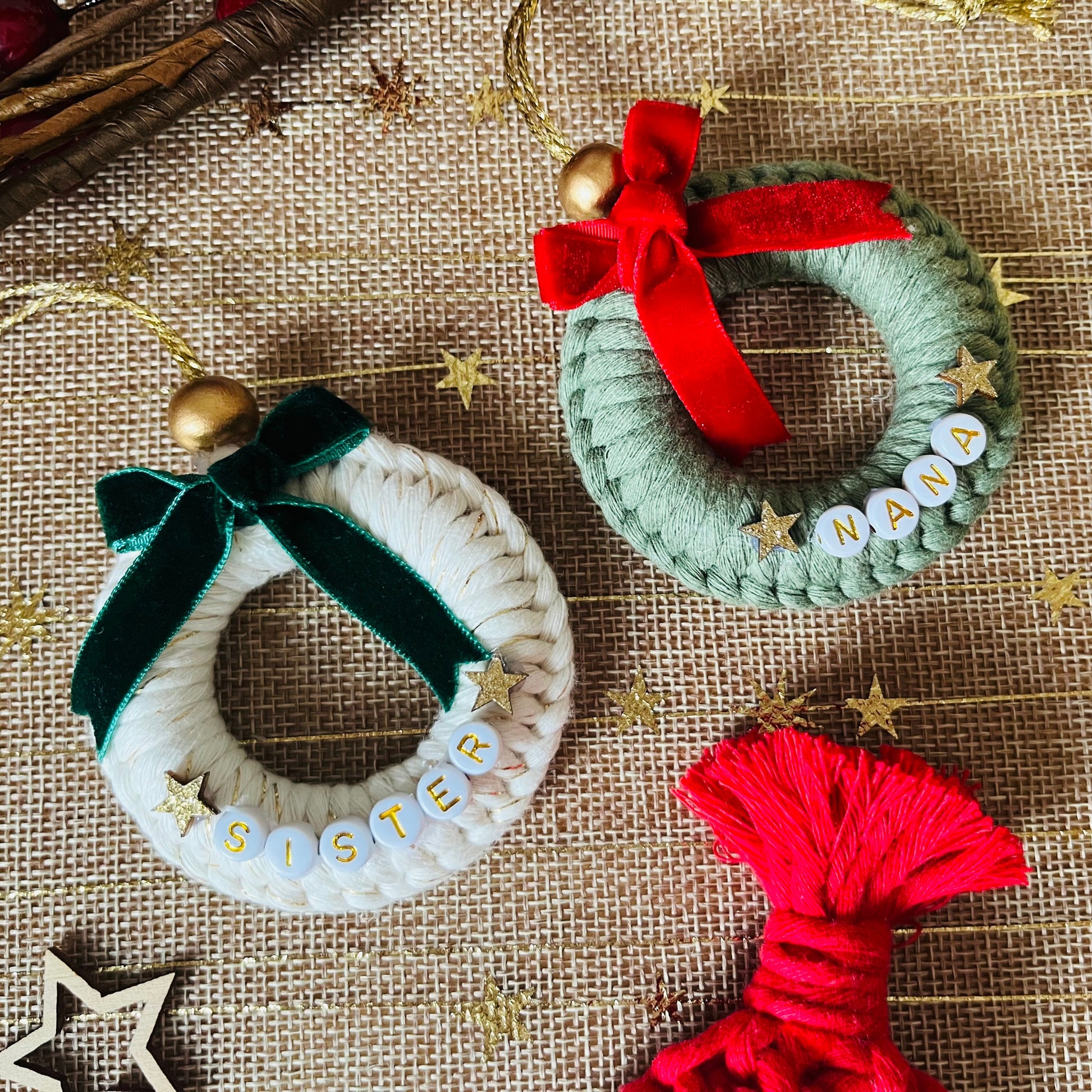 Two yarn-wrapped wreath ornaments with ribbons on a textured surface with decorative stars.