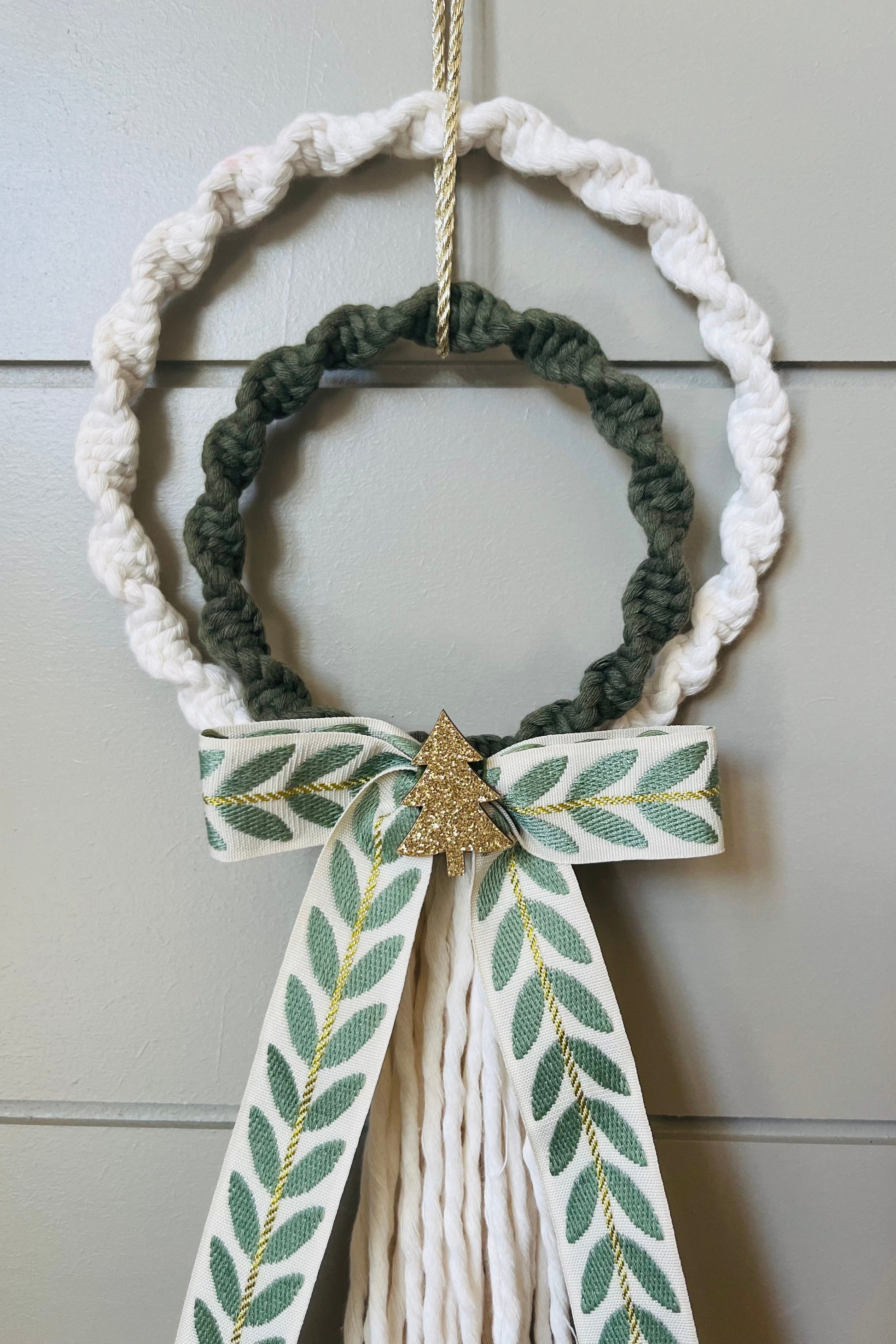 Decorative macrame Christmas wreath with tassels and a bow on a plain background