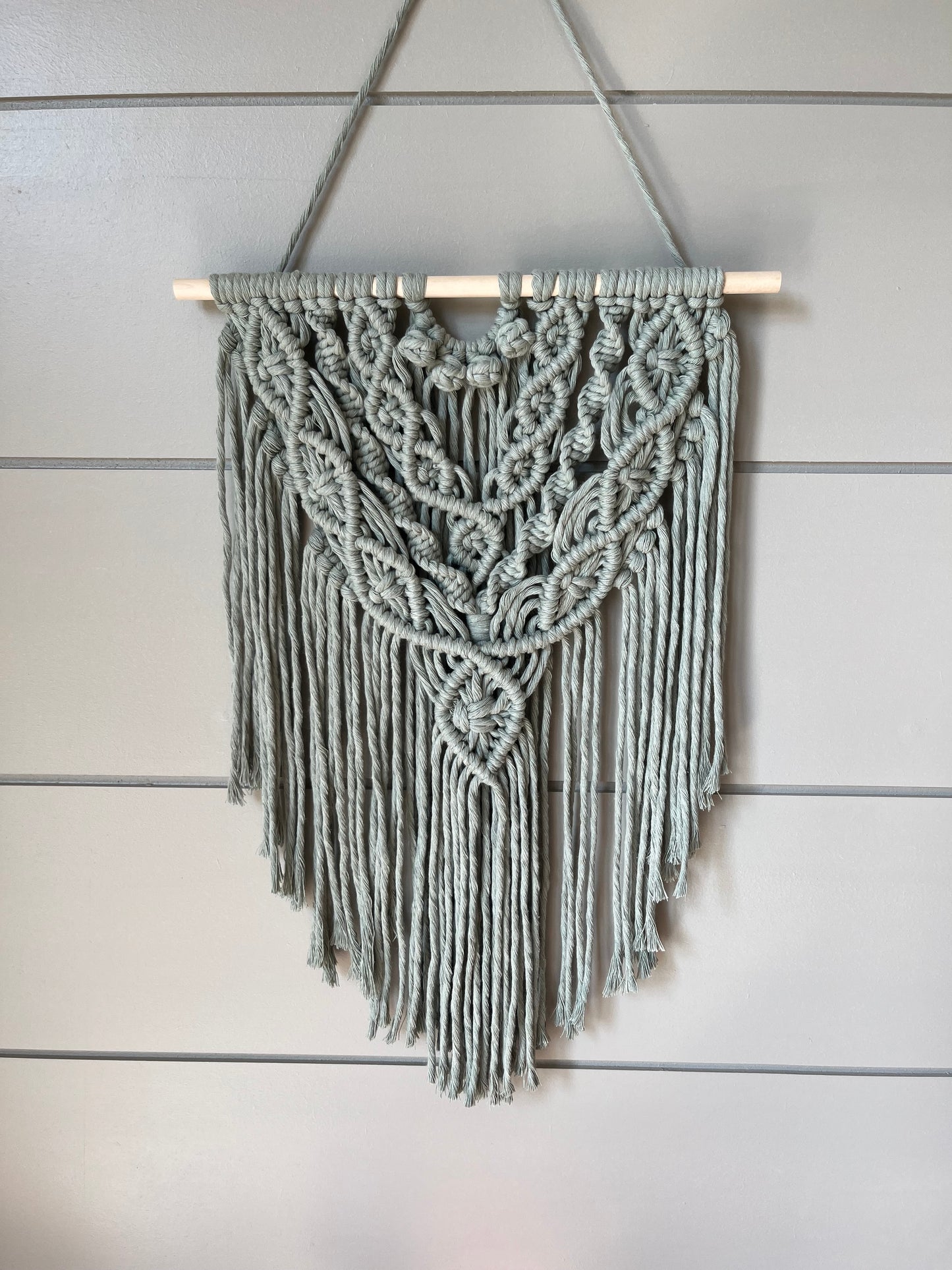 Decorative macramé boho wall hanging on a wooden panel background in sage