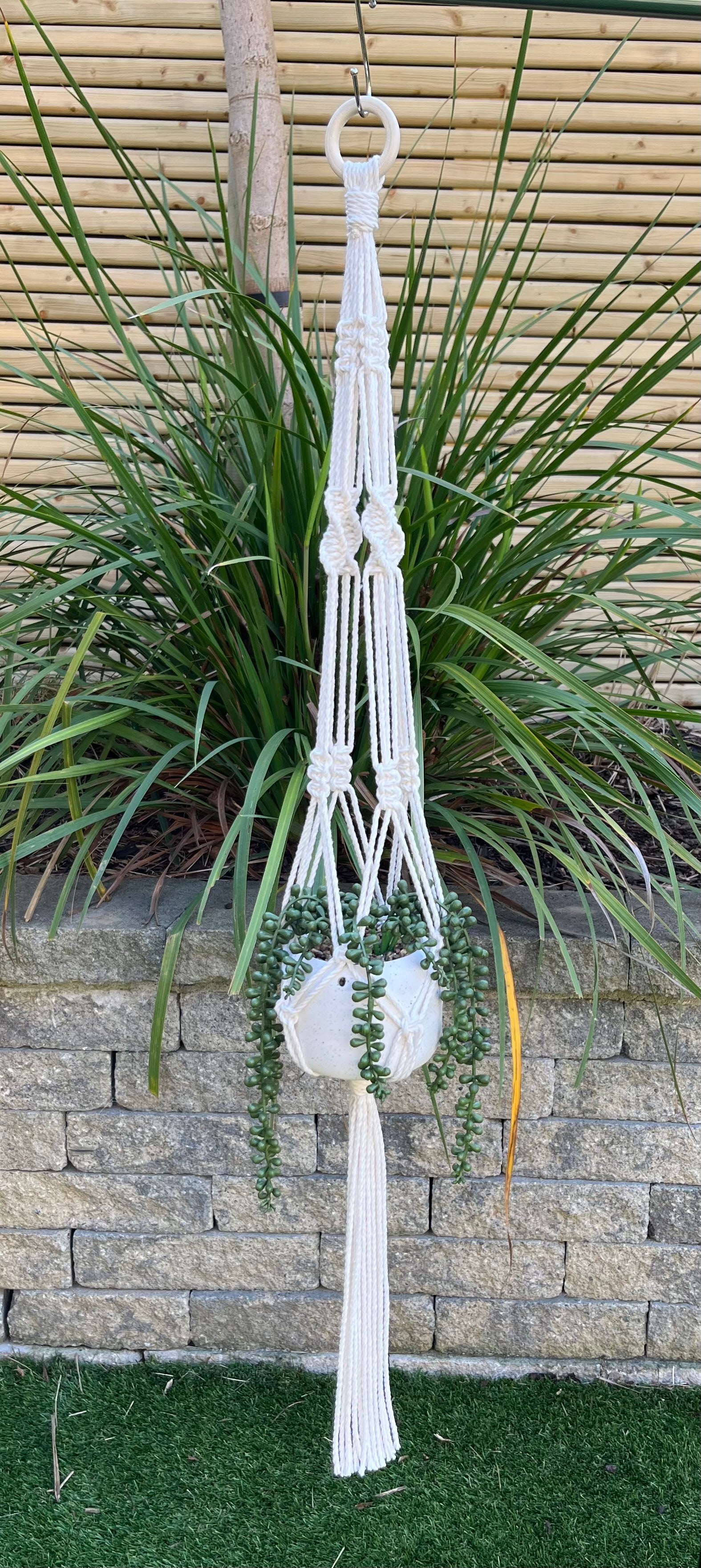 Macramé plant hanger in natural colour with a gold pot against a garden background.