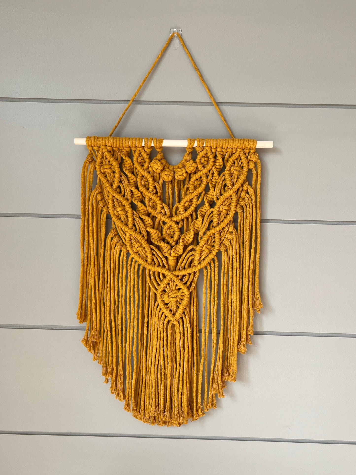 Decorative macramé boho wall hanging on a wooden panel background in mustard