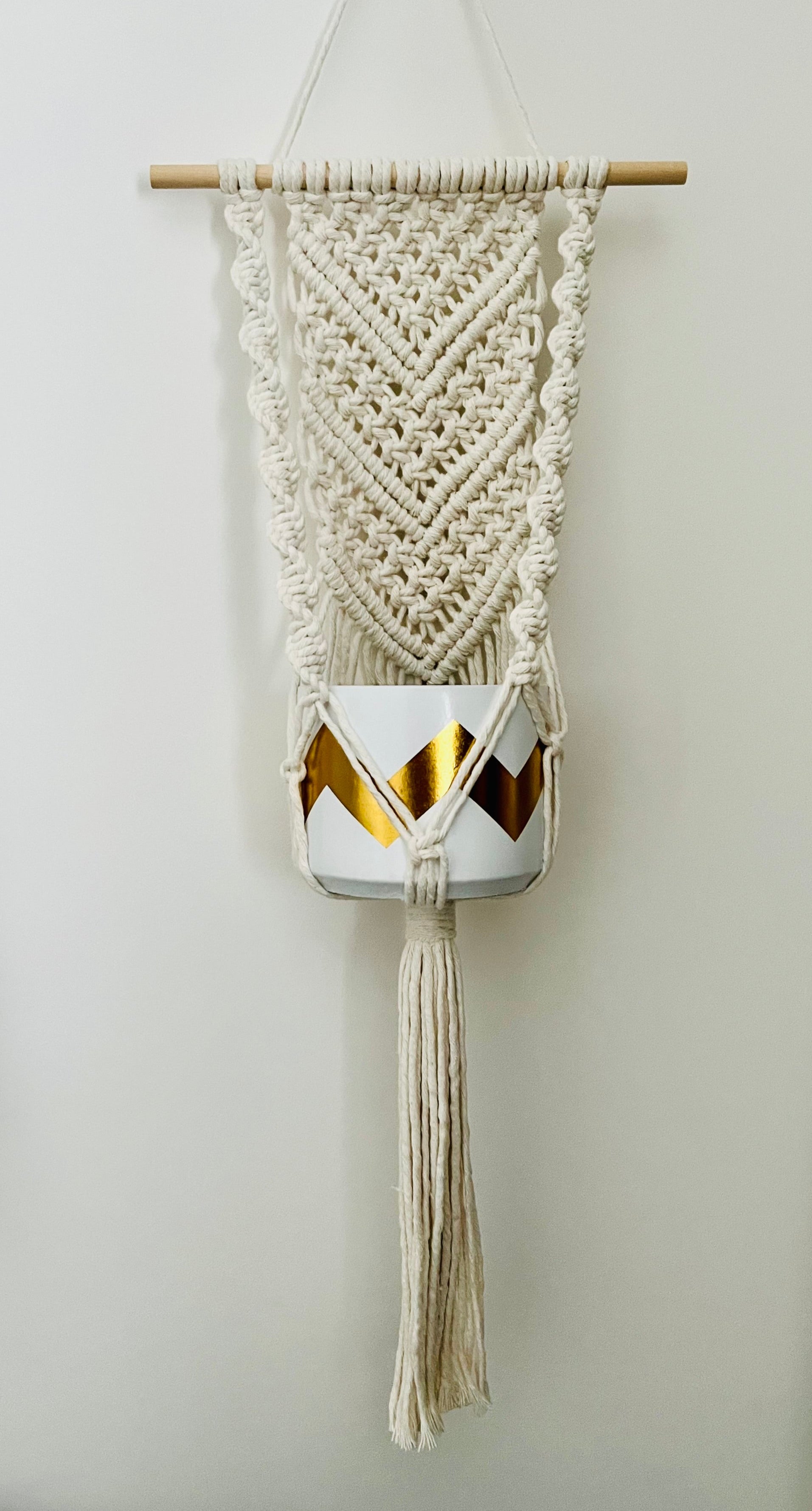 Macramé wall hanging plant hanger with geometric pattern and tassels on a plain background