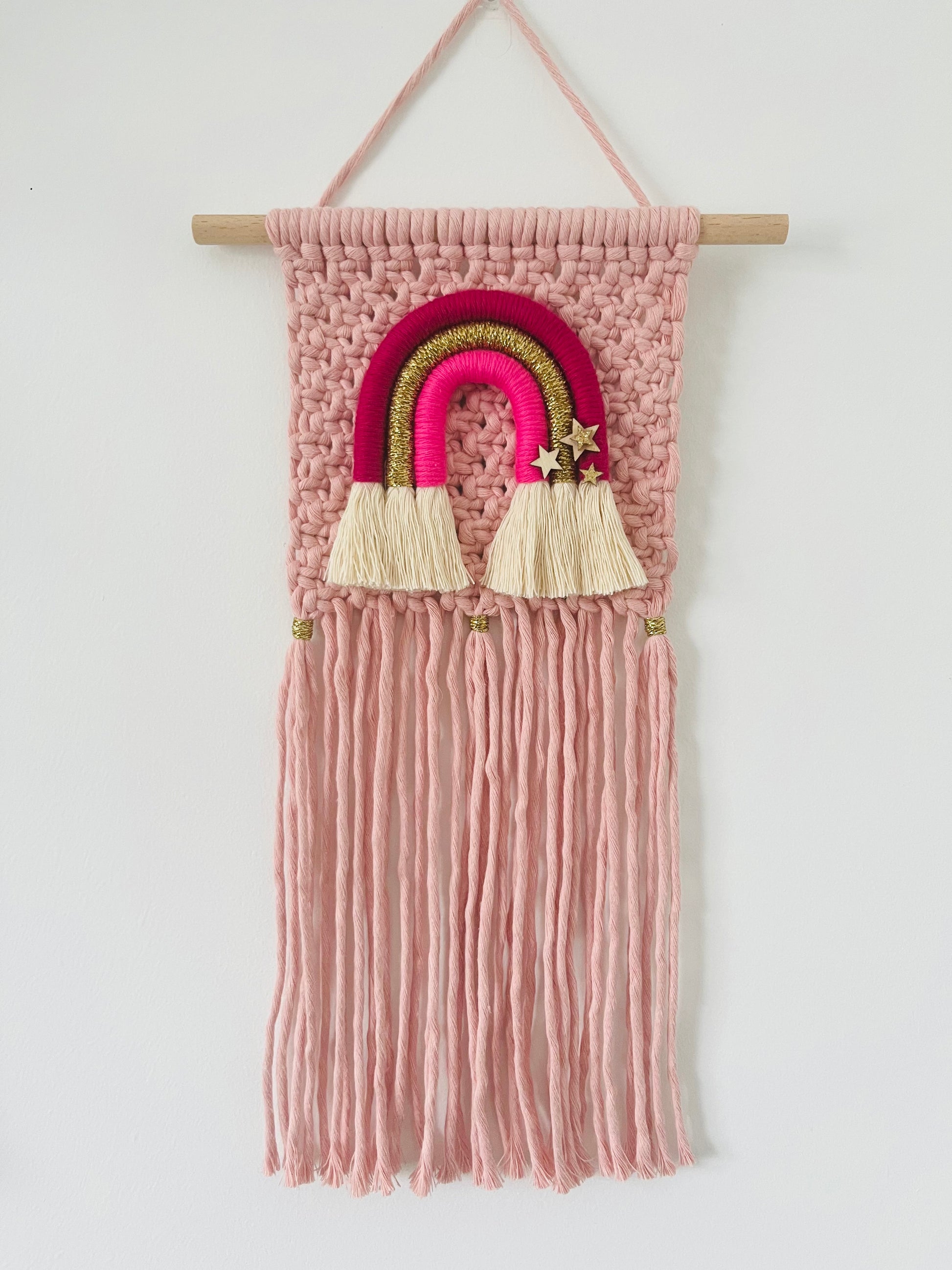 Macramé wall hanging in pink with coordinating rainbow design and fringing