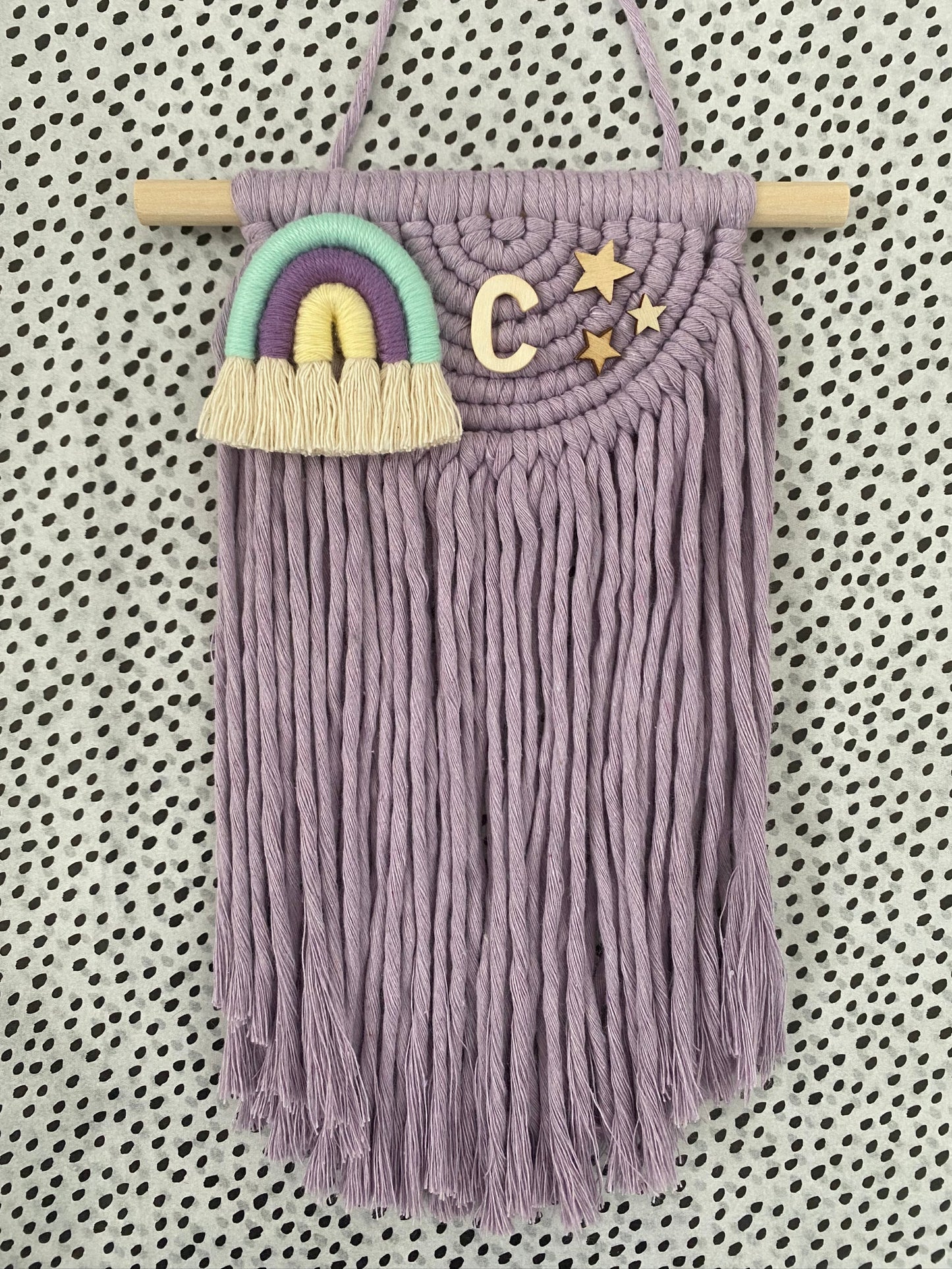 Decorative macramé wall hanging with fringing and a colorful rainbow on a patterned background