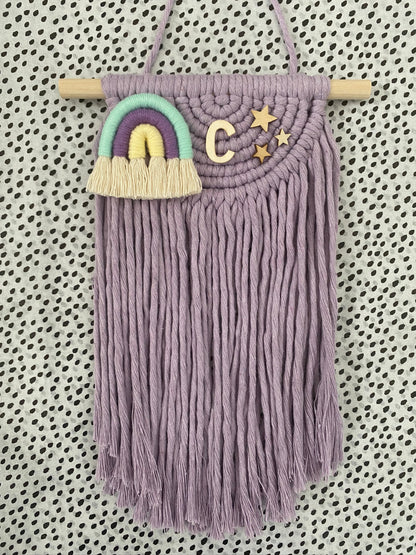 Decorative macramé wall hanging with fringing and a colorful rainbow on a patterned background
