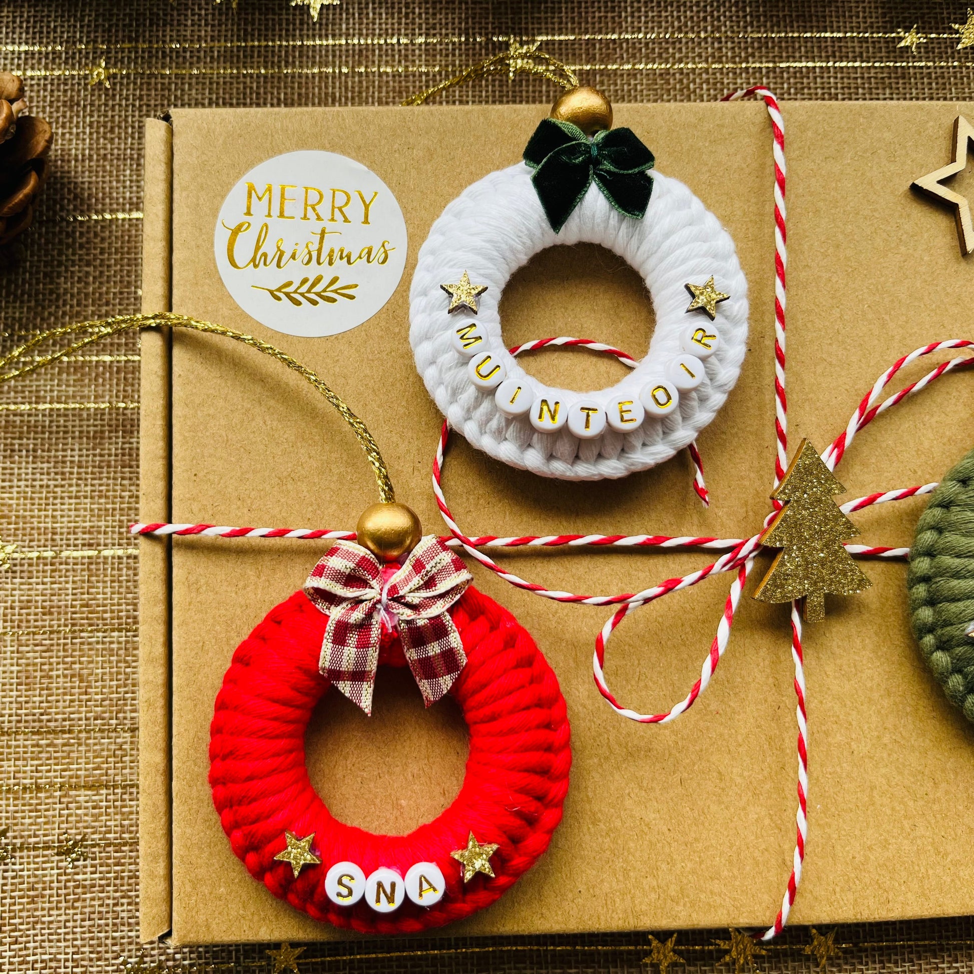 Decorative macrame wreaths on a brown box with 'Merry Christmas' label, pine cone, and string on a textured background.