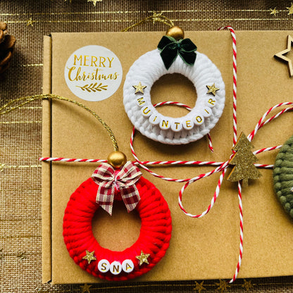 Decorative macrame wreaths on a brown box with 'Merry Christmas' label, pine cone, and string on a textured background.
