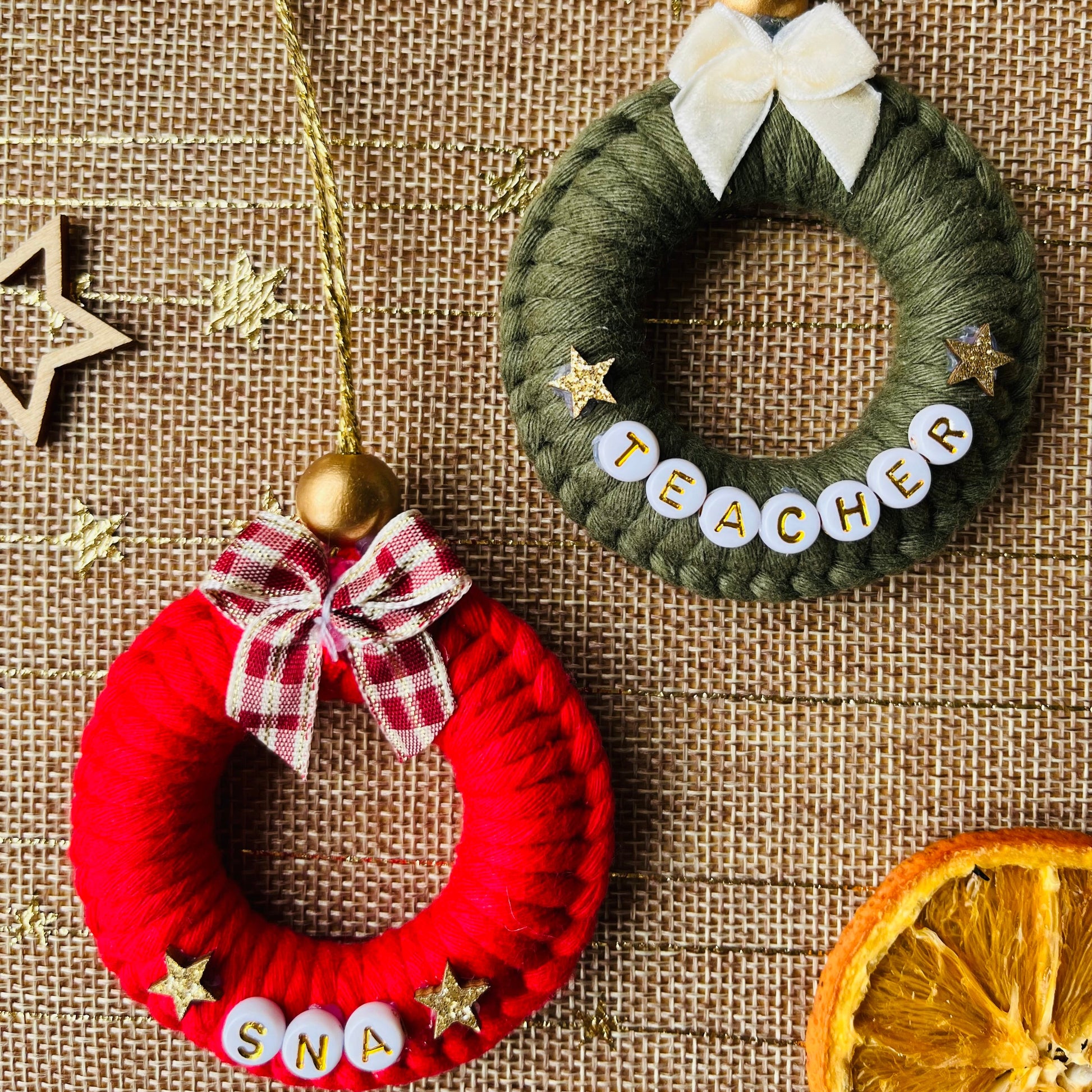 Two small wreath ornaments, one red and one green, on a textured surface with decorative elements.