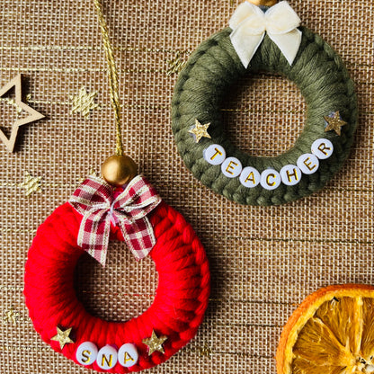 Two small wreath ornaments, one red and one green, on a textured surface with decorative elements.