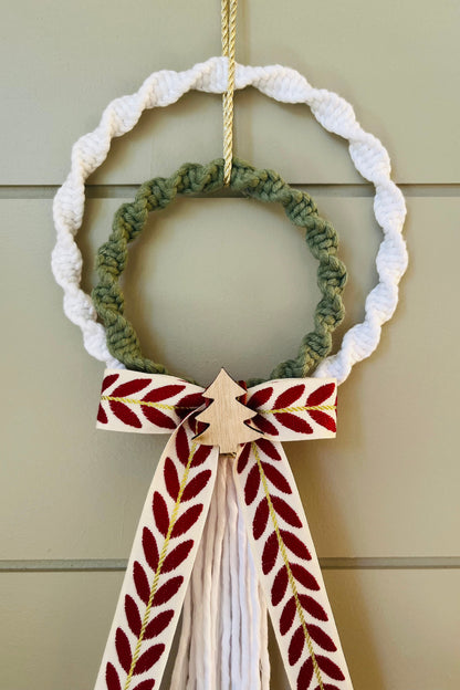 Decorative macrame Christmas wreath with tassels and a bow on a plain background