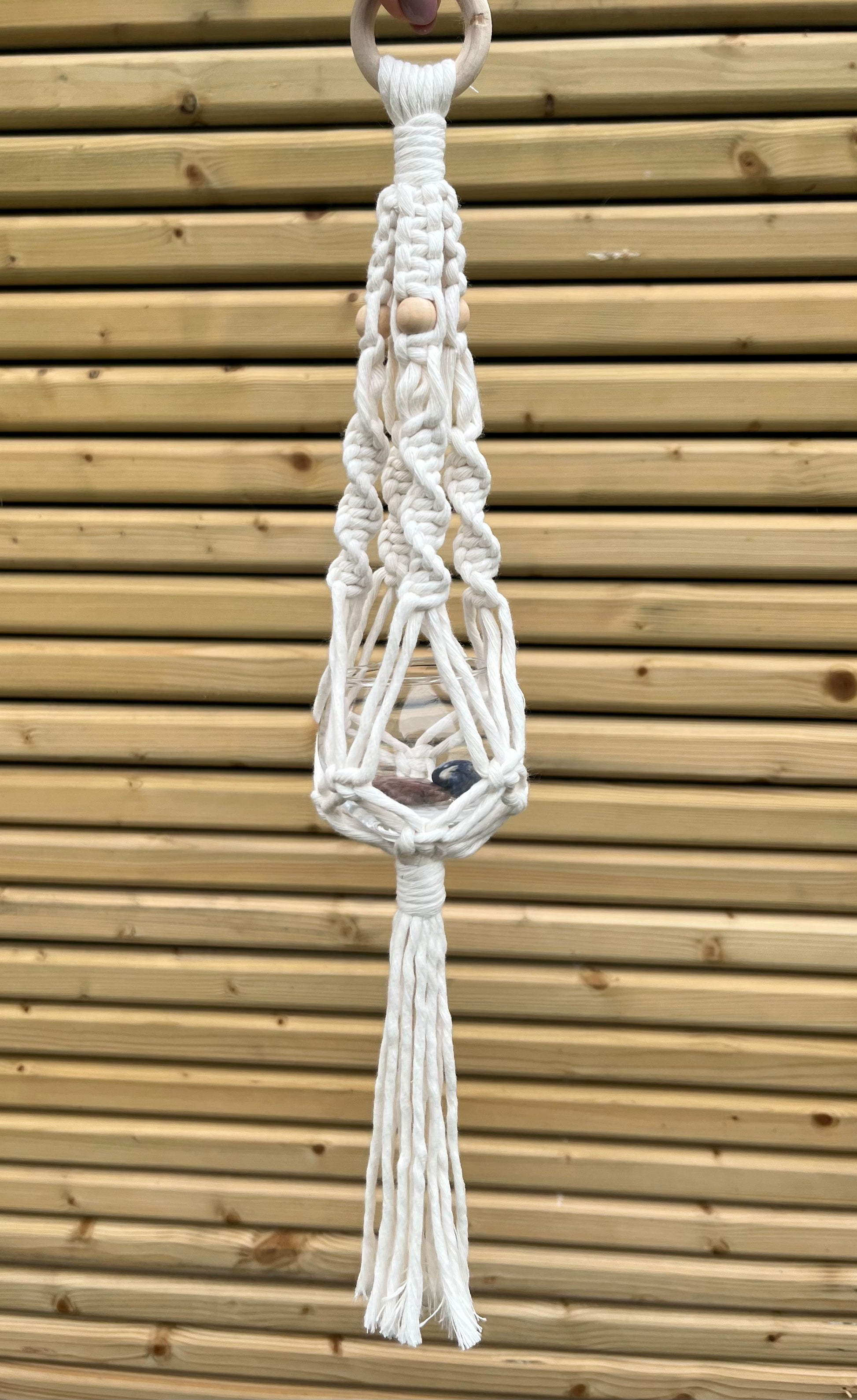 Macrame pot hanger hanging against a wooden background