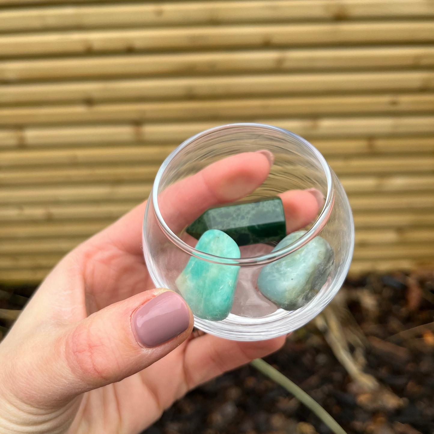 Hand holding a small glass container with green crystals against a natural background