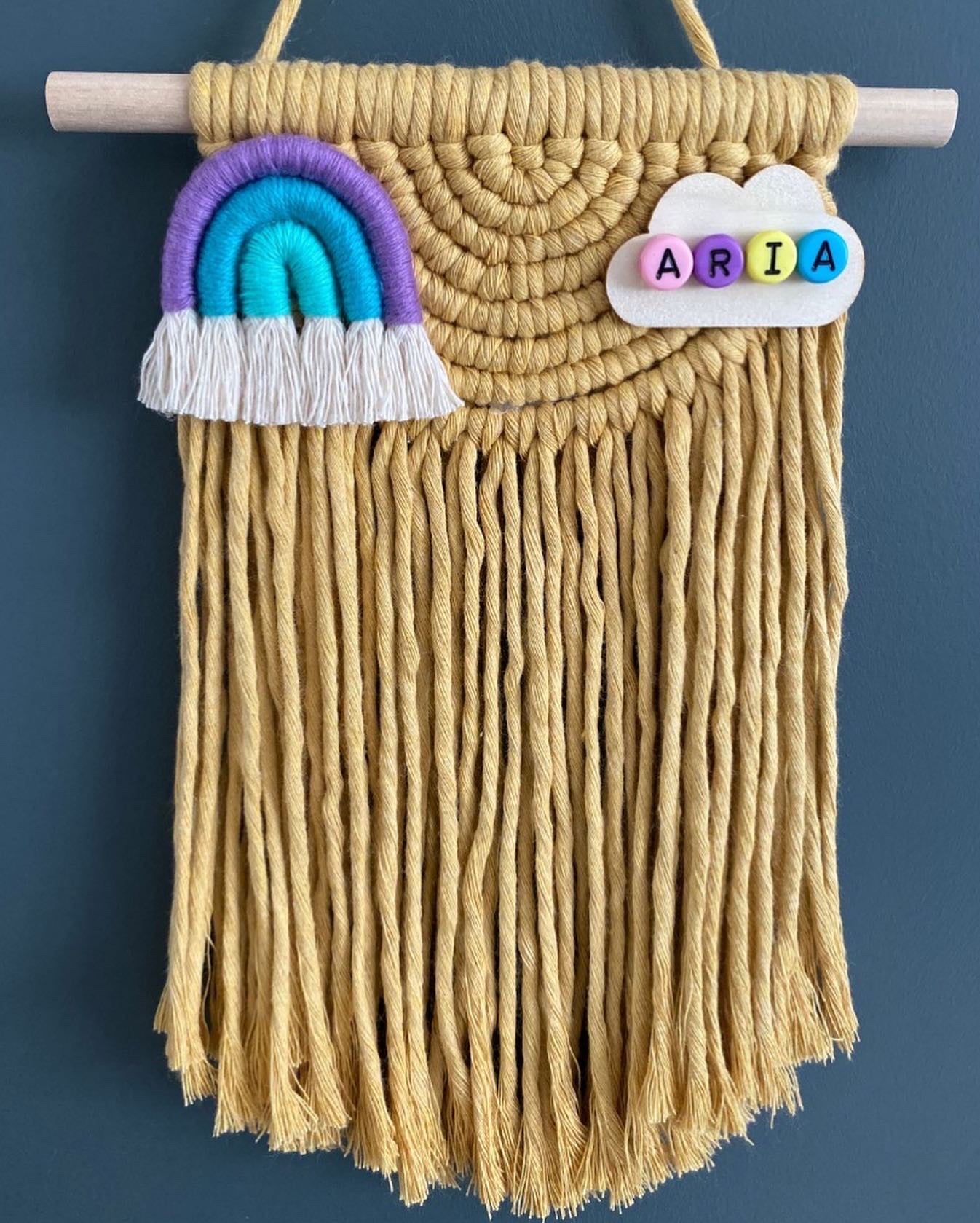 Macramé wall hanging with rainbow and cloud design on a blue background