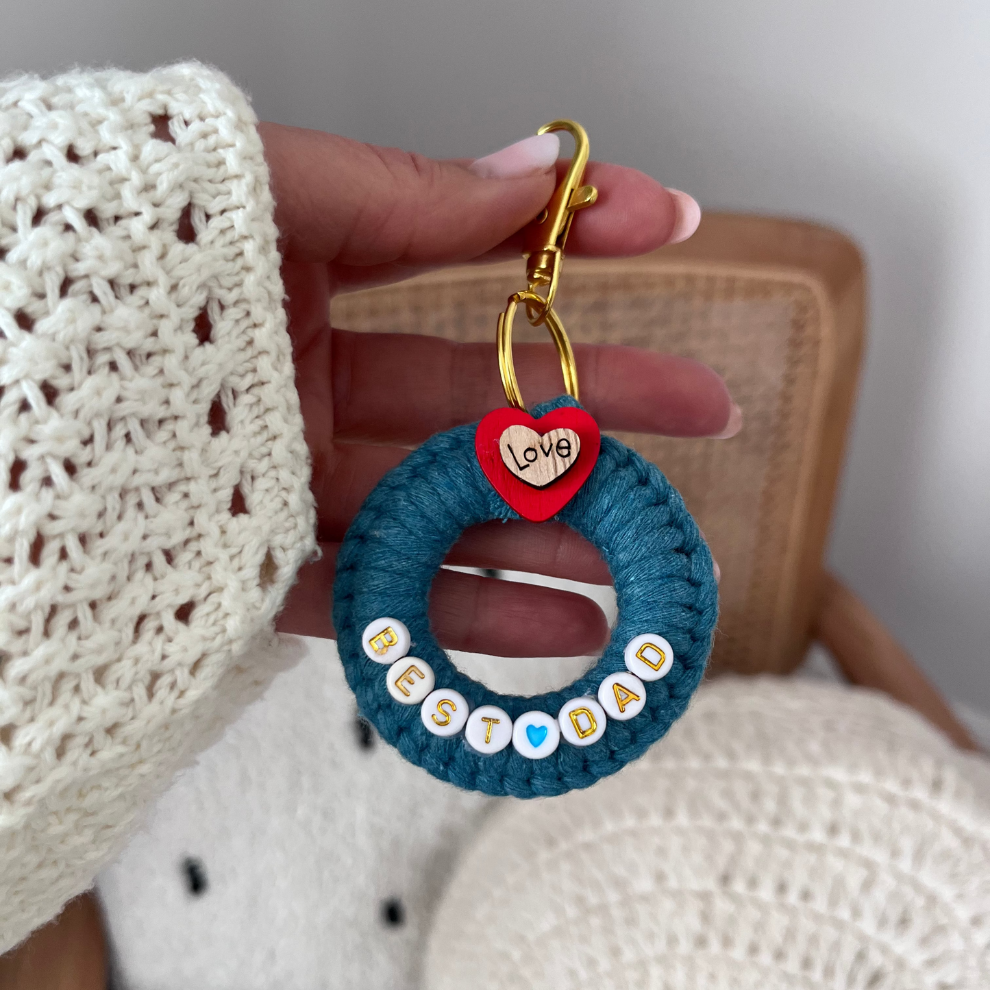Hand holding a blue crocheted keychain with 'Best Dad' text and heart-shaped tag.