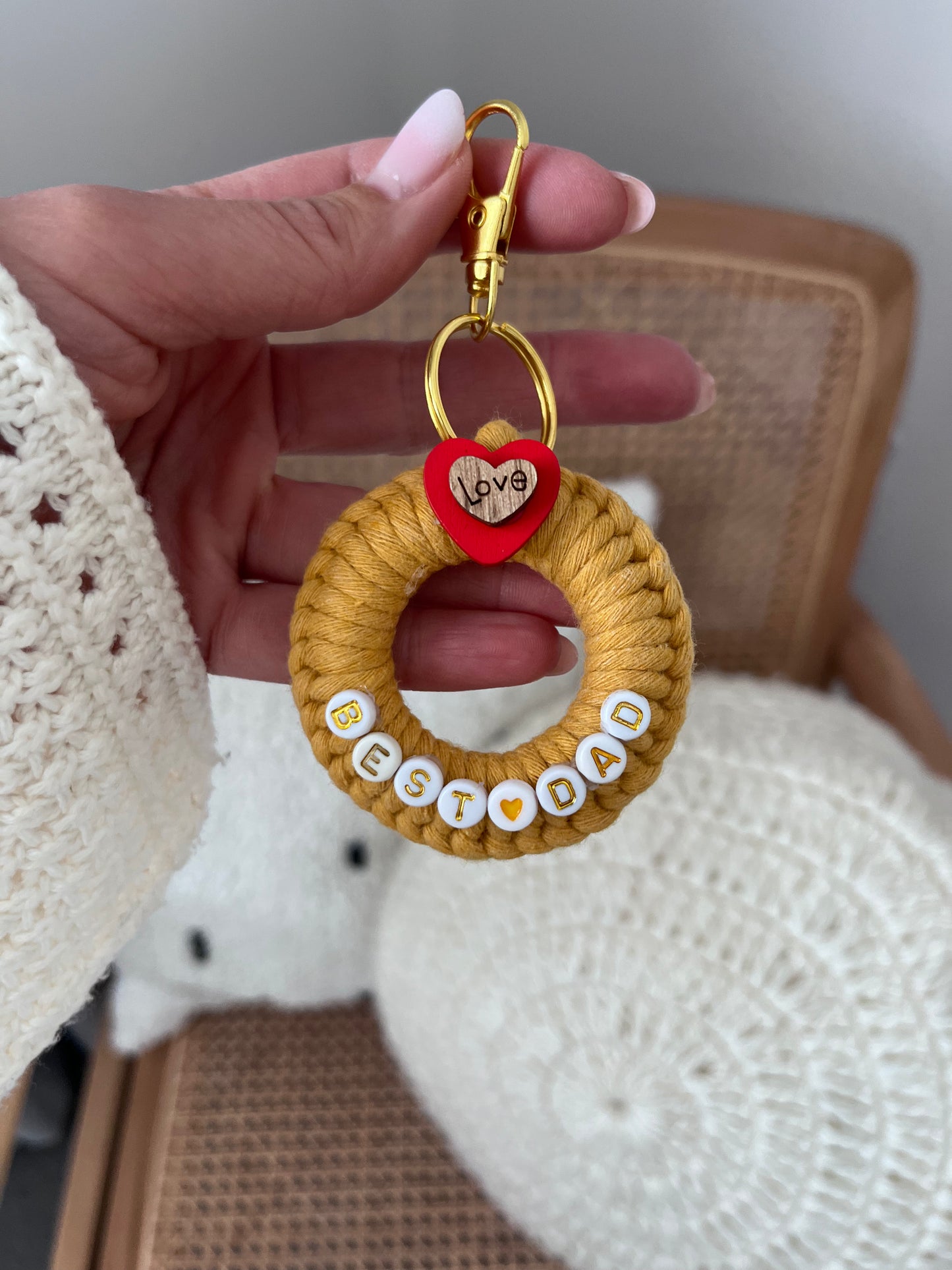 Hand holding a keychain with 'Best Dad' text and a heart-shaped tag, with a blurred background.