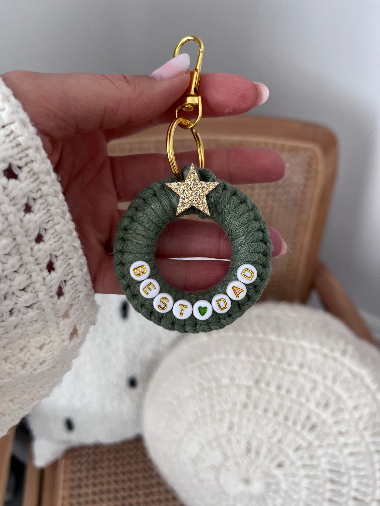 Hand holding a green crocheted keychain with 'BEST DAD' text and a star charm.