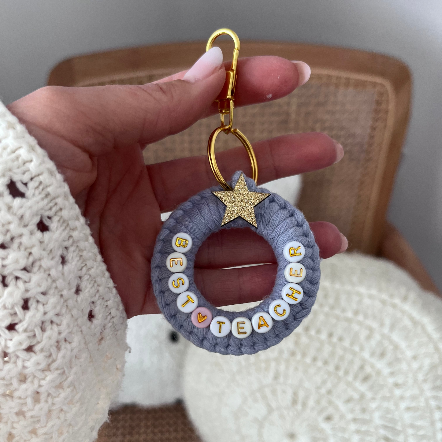 Hand holding a keychain with 'Best Teacher' text against a neutral background