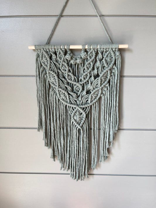Decorative macramé boho wall hanging on a wooden panel background in sage