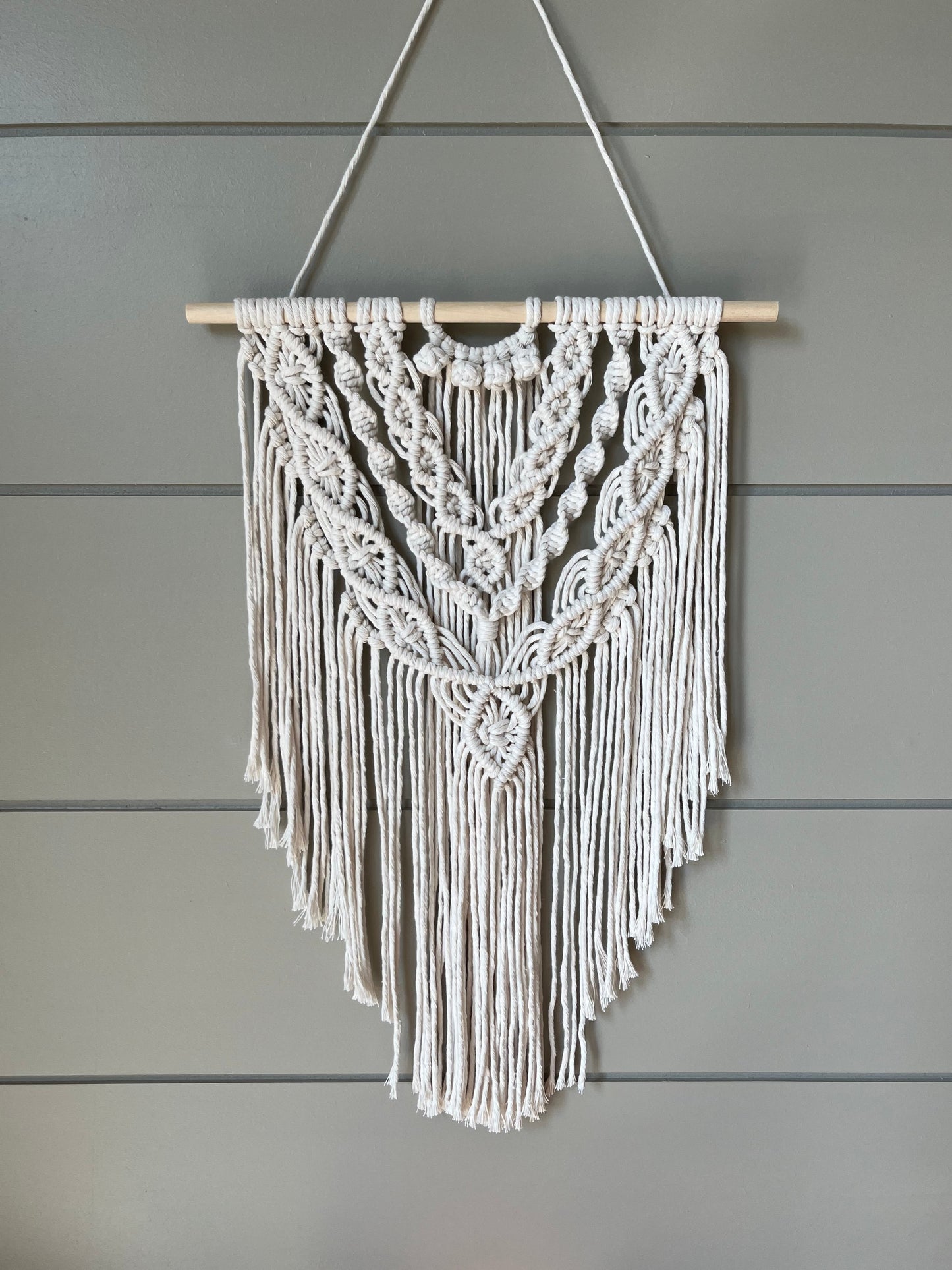 Decorative macramé boho wall hanging on a wooden panel background in natural