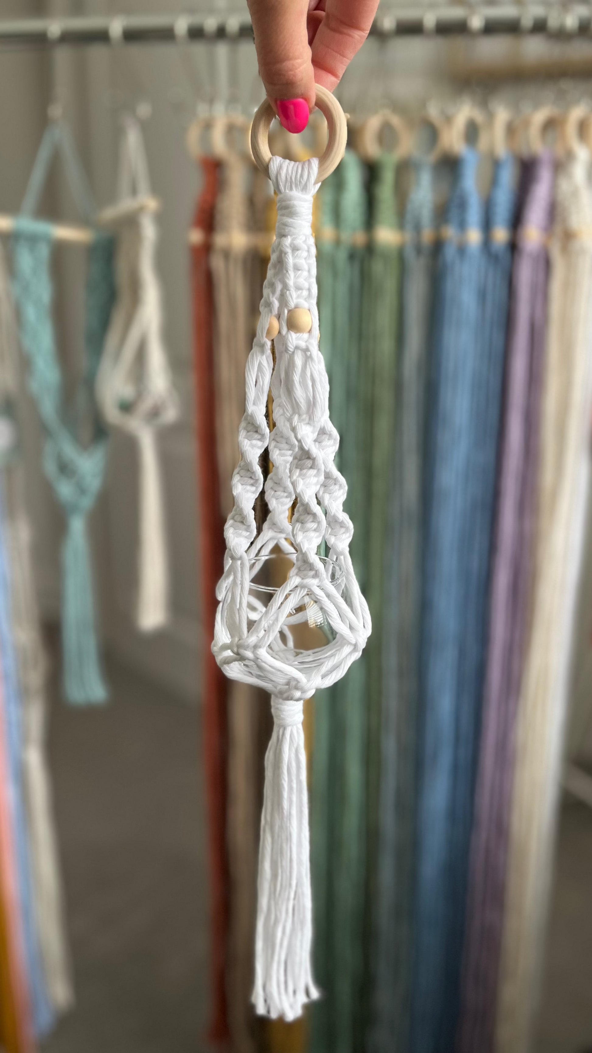 White macrame crystal hanger with a  wooden ring held by a hand against a colorful fabric background.