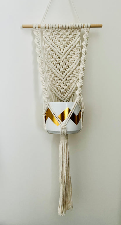 Macramé wall hanging plant hanger with geometric pattern and tassels on a plain background