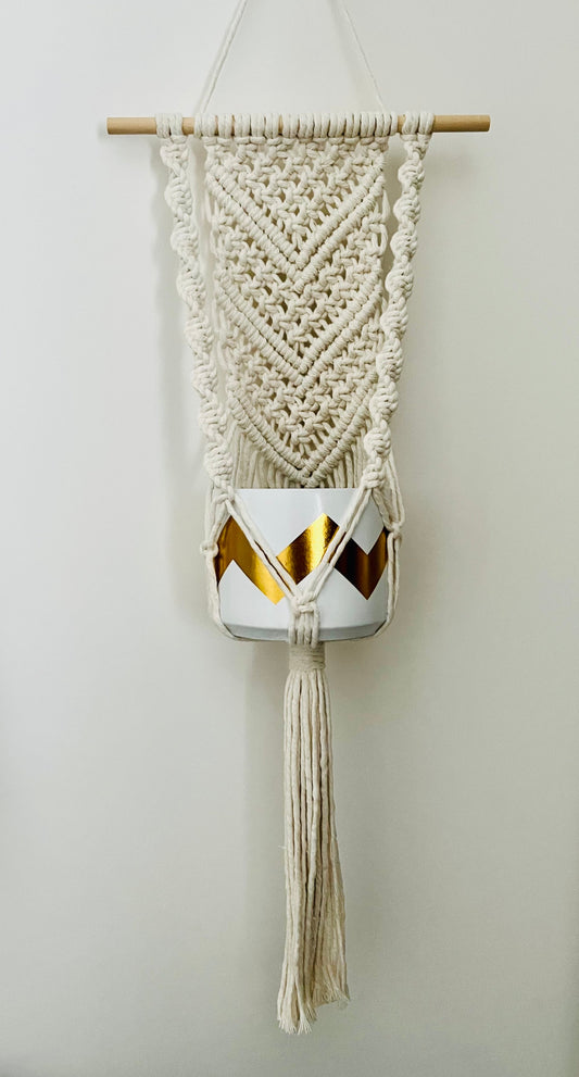 Macramé wall hanging plant hanger with geometric pattern and tassels on a plain background