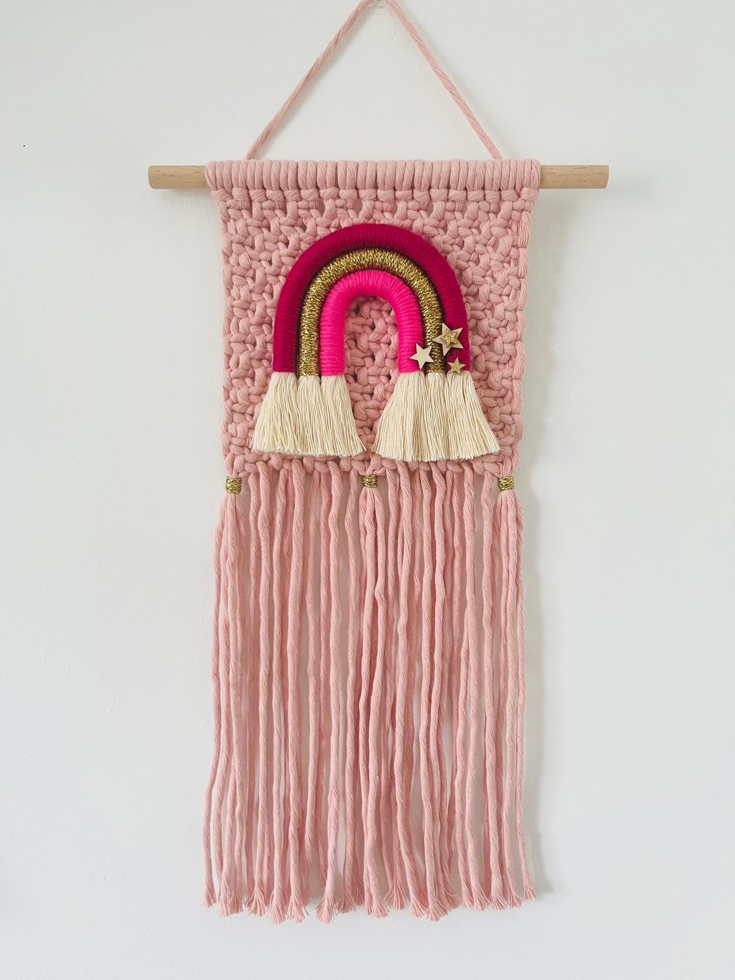 Macramé wall hanging in pink with coordinating rainbow design and fringing