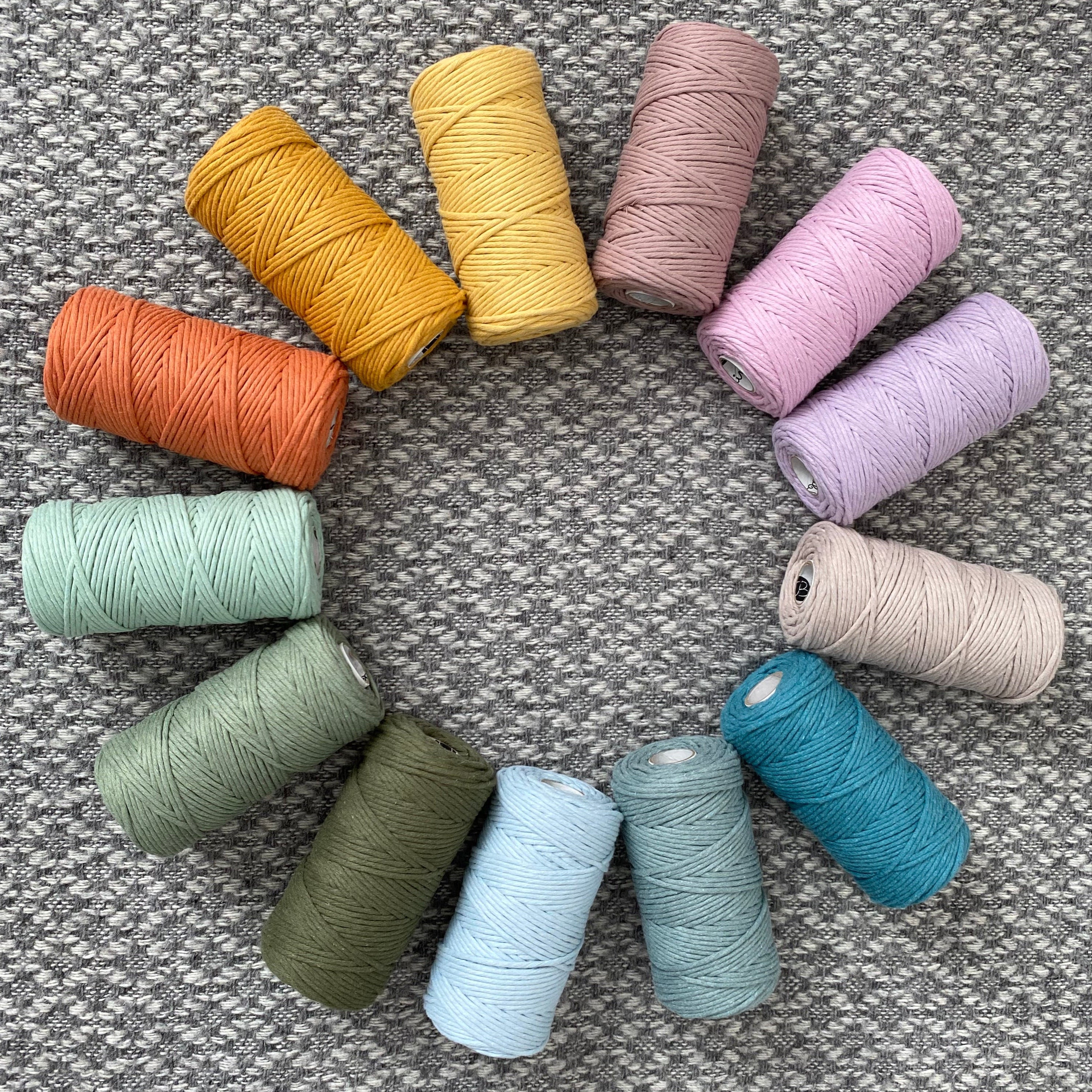 Assorted colorful macramé cord arranged in a circle on a textured surface.