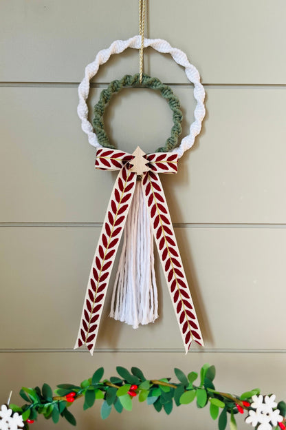 Decorative macrame Christmas wreath with tassels and a bow on a plain background
